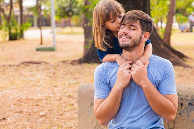 Padre e figlia sorridono alla telecamera nel parco La figlia si arrampica sulla schiena di papà Happy Fathers Day