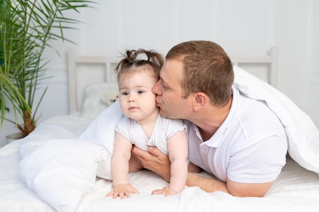 Padre e figlia sul letto sotto la coperta che baciano e abbracciano Buona festa del papà in famiglia