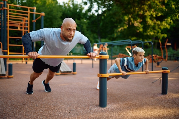 Padre e figlio che fanno esercizio, allenamento sportivo nel parco giochi all'aperto. La famiglia conduce uno stile di vita sano, allenamento fitness nel parco estivo