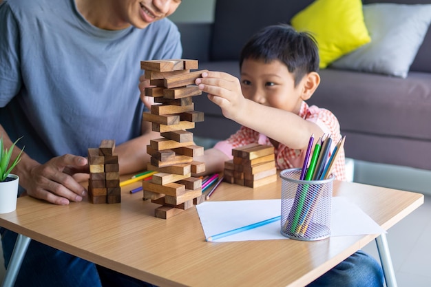 Padre e figlio che giocano a blocchi di legno o a un gioco di jenga a casa nel fine settimana. Giochi educativi per bambini. Felicità familiare e attività insieme a casa concept