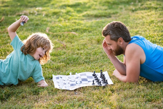 Padre e figlio che giocano a scacchi sdraiati sull'erba al parco del prato la festa del papà ama la genitorialità della famiglia