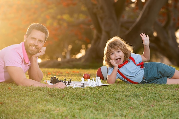 Padre e figlio che giocano a scacchi sdraiati sull'erba al parco giochi e intrattenimento per la famiglia dei bambini