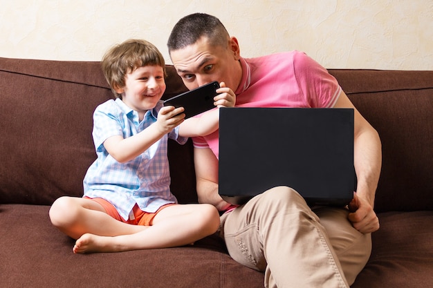 Padre e figlio con laptop e telefono cellulare a casa