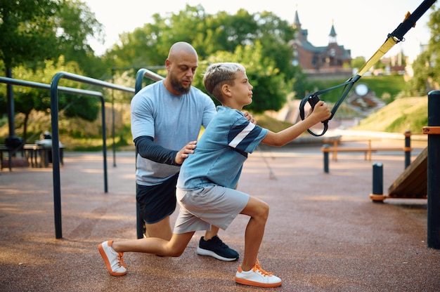 Padre e figlio, esercizio con le corde, allenamento sportivo nel parco giochi all'aperto. La famiglia conduce uno stile di vita sano, allenamento fitness nel parco estivo