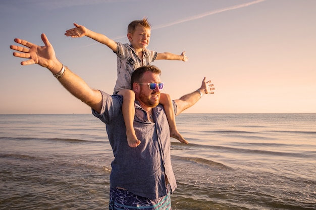 Padre e figlio felici che hanno tempo della famiglia sulla spiaggia sul tramonto