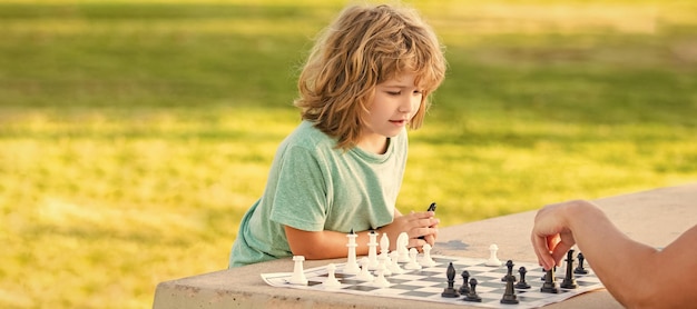 Padre e figlio giocano a scacchi banner all'aperto poster con spazio copia figlio bambino che gioca a scacchi sul tavolo nel parco all'aperto con suo padre infanzia