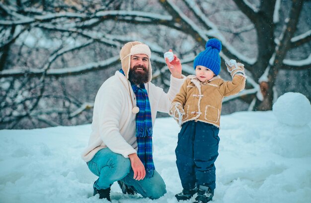 Padre e figlio giocano con la palla di neve su uno sfondo bianco invernale. Scena invernale su uno sfondino bianco nevoso.