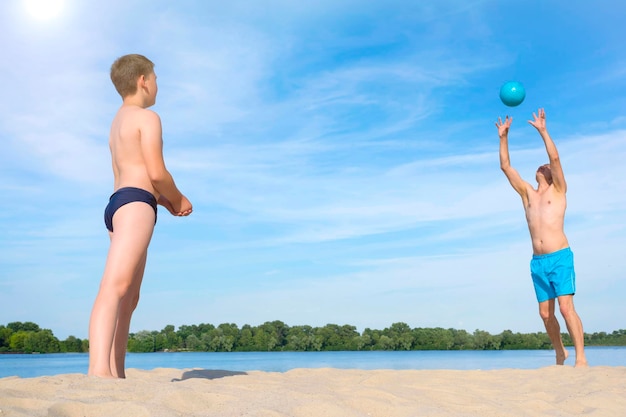 Padre e figlio giocano con la palla nella sabbia Giochi sportivi sulla spiaggia in una soleggiata giornata estiva