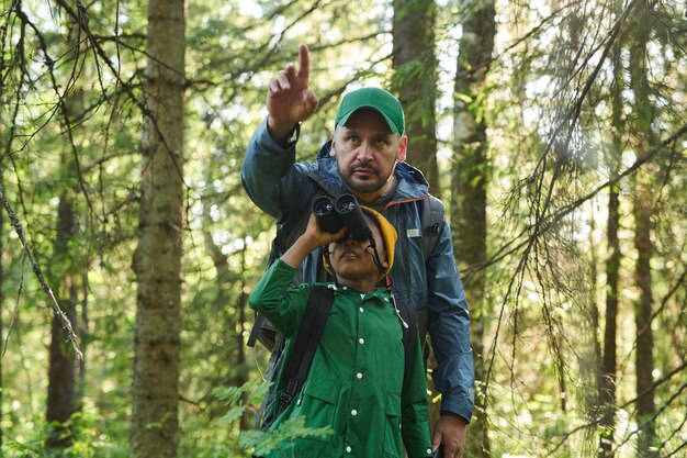 Padre e figlio in piedi nella foresta e usando il binocolo per guardare la splendida vista