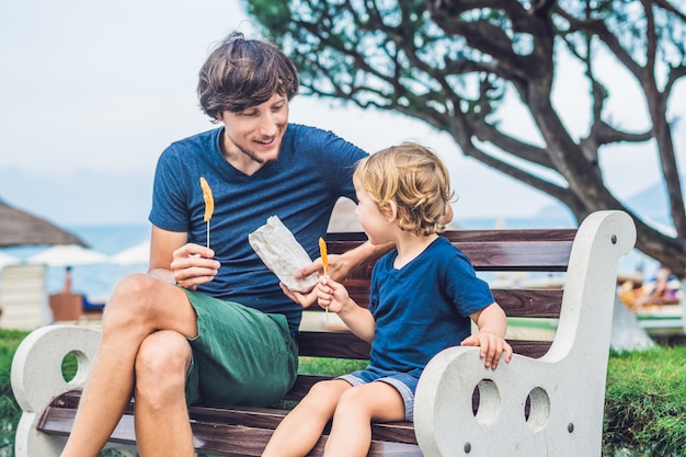 Padre e figlio mangiano patate dolci fritte nel parco in panchina