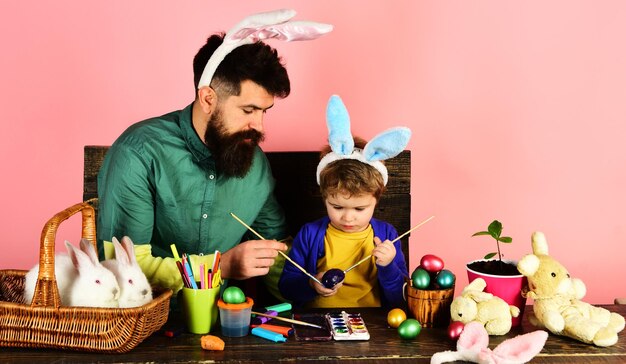 Padre e figlio piccolo che dipingono le uova di pasqua famiglia felice in orecchie di coniglio che si preparano per le vacanze