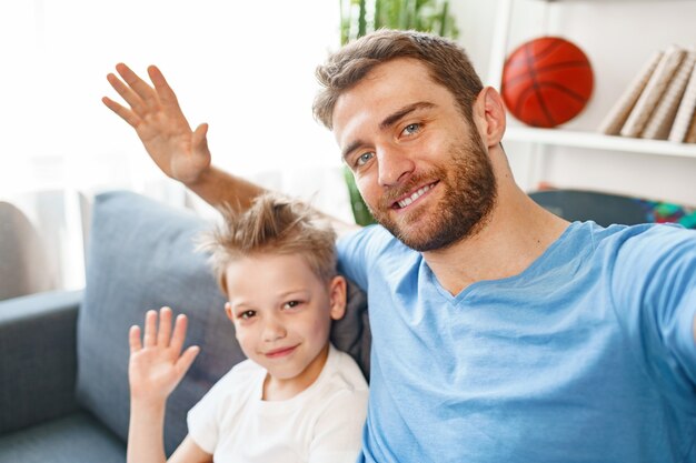 Padre e figlio seduti sul divano e agitando le mani verso la telecamera a casa