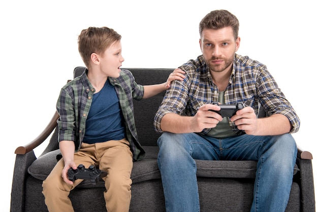 Padre e figlio seduti sul divano e giocando con i joystick isolati su bianco