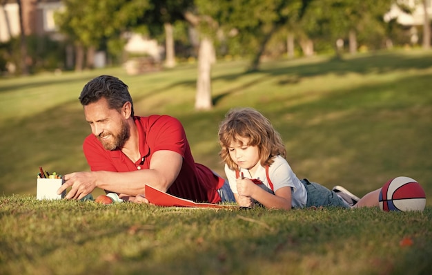 Padre e figlio si rilassano sull'erba nel parco imparando a disegnare tutoraggio