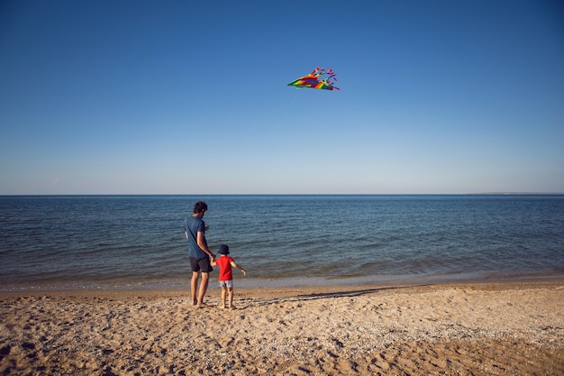 Padre e figlio sono in piedi su una spiaggia sabbiosa in riva al mare e lanciano un aquilone a strisce giocattolo in estate in vacanza