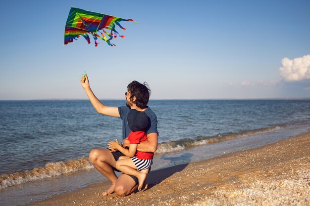 Padre e figlio sono in piedi su una spiaggia sabbiosa in riva al mare e lanciano un aquilone a strisce giocattolo in estate in vacanza