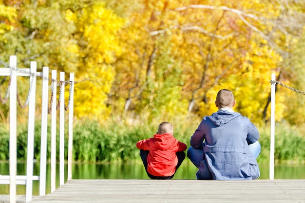 Padre e figlio sono seduti sul molo Autunno soleggiato Vista posteriore