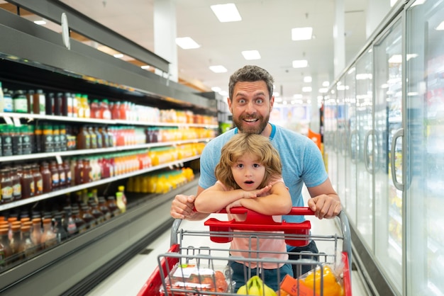 Padre e figlio sorridenti felici con il carrello della spesa che comprano cibo al supermercato o al supermercato