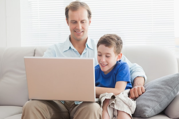 Padre e figlio usando il portatile sul divano