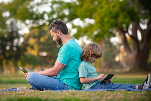 Padre e figlio usano il computer portatile, il papà e il bambino della scuola cercano l'apprendimento a distanza all'aperto con tablet