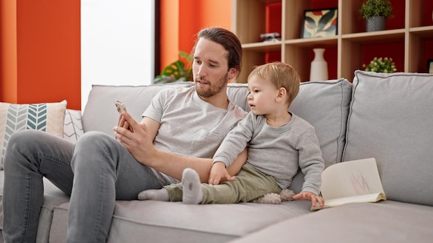 Padre e figlio utilizzano lo smartphone seduti insieme sul divano a casa