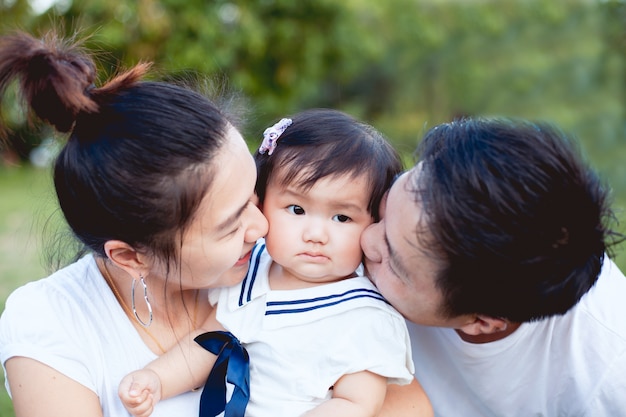 Padre e madre della famiglia asiatica che bacia figlia e che giocano insieme nel parco