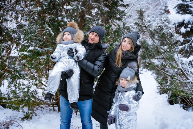 Padre e madre tengono i bambini tra le braccia che ridono allegramente passeggiata invernale in famiglia nella foresta raisi...