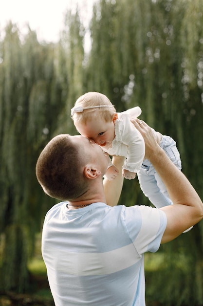 Padre e piccola figlia in piedi nel parco e in posa per una foto. Famiglia vestita di bianco e azzurro