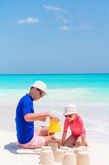 Padre e piccole figlie che fanno il castello di sabbia alla spiaggia tropicale