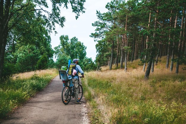 Padre e suo figlio che viaggiano in bicicletta nella foresta la ragazza è seduta nel seggiolino