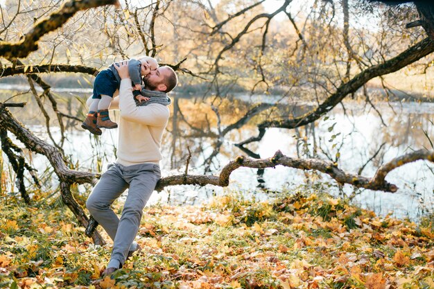 Padre felice che gioca con il suo piccolo bambino nel parco di autunno