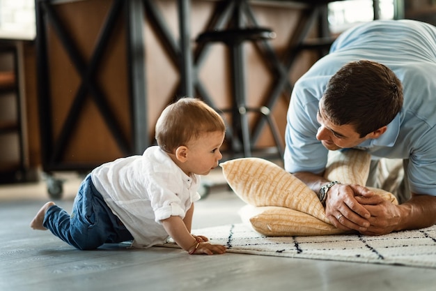 Padre felice che parla con suo figlio piccolo che sta strisciando sul pavimento del soggiorno