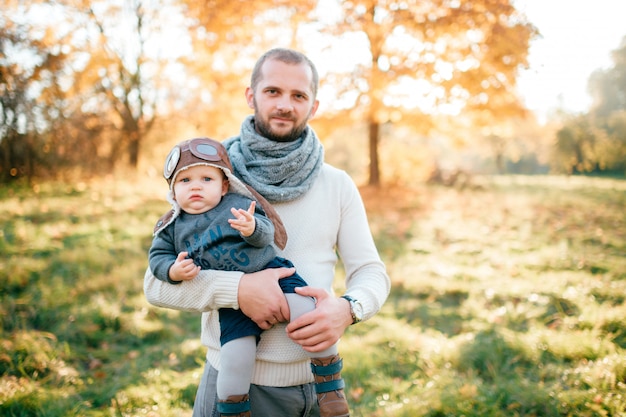 Padre felice che posa con il suo bambino alla moda nel parco di autunno