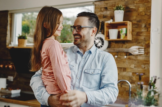 Padre felice che si diverte mentre tiene in braccio sua figlia e comunica con lei in cucina