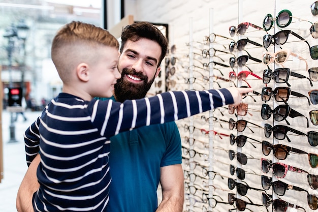 Padre felice e figlio che scelgono gli occhiali da sole nel negozio di ottica.