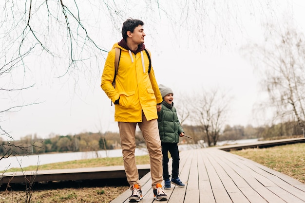 Padre in impermeabile giallo e figlio che si divertono nella foresta famiglia felice con un bambino che gioca e