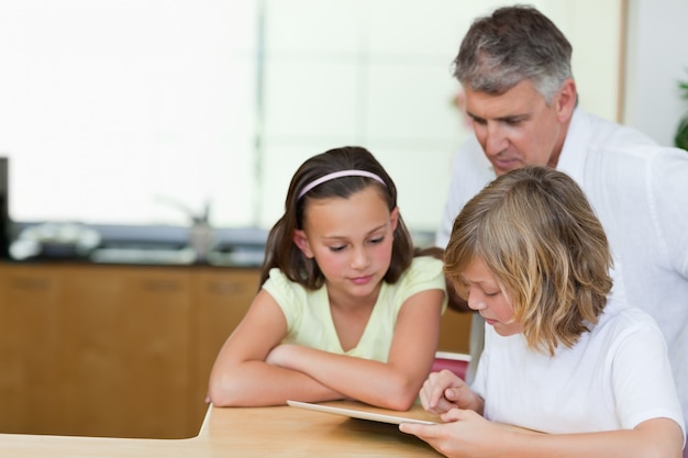 Padre insieme a bambini e tablet in cucina