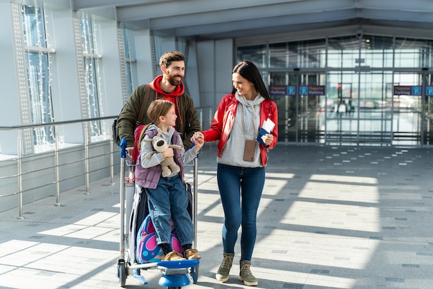 Padre madre e figlia si preparano per il volo mentre si trovano nella sala partenze con le valigie e aspettano l'arrivo dell'aereo