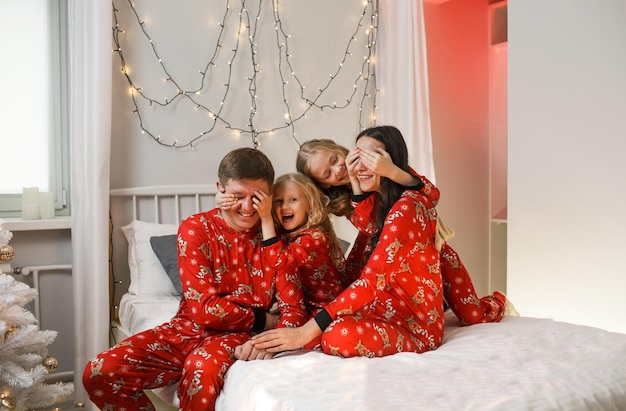 Padre mamma e due figlie piccole si divertono a letto. Famiglia felice in pigiama di Natale rosso in camera da letto la mattina di Natale. Capodanno