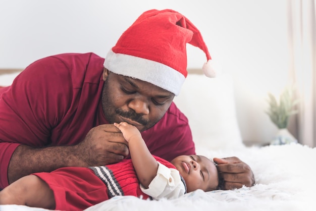 Padre nigeriano che indossa un cappello rosso di Natale e bacia la mano del figlio neonato di 4 mesi