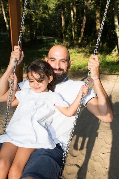 Padre oscillante con la figlia bambina in un parco giochi