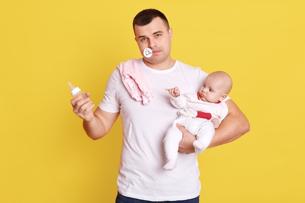 Padre preoccupato con il suo bambino appena nato, cercando di nutrire il bambino, indossa una maglietta casual bianca