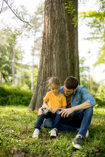 Padre single che si siede sull'erba dall'albero con la piccola figlia