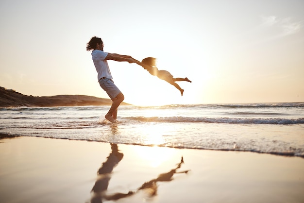 Padre spin ragazza bambino e spiaggia con giochi tenendosi per mano o tramonto per legare insieme dalle onde Papà bambina e dondola per amore cura o gioca in riva al mare silhouette o famiglia in vacanza in estate