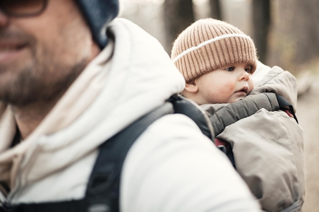 Padre sportivo che porta suo figlio neonato indossando una tuta invernale e un berretto in un portabagagli che fa escursioni in