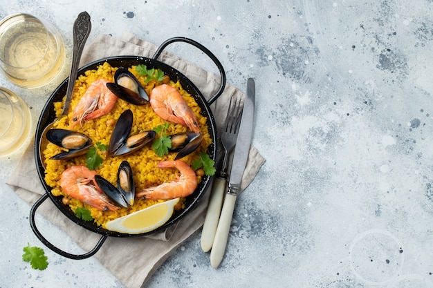 Paella spagnola tradizionale dei frutti di mare in padella con ceci, gamberetti, cozze, calamari su fondo di cemento grigio chiaro. Vista dall'alto con copia spazio