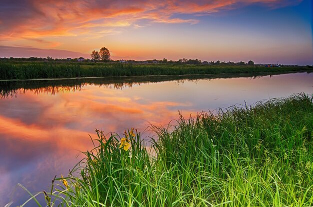 Paesaggio al tramonto estivo rurale con fiume e cielo colorato drammatico