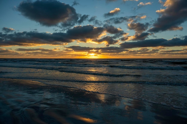 Paesaggio al tramonto sull'oceano con morbide onde di acqua di mare serali che si schiacciano sulla spiaggia sabbiosa