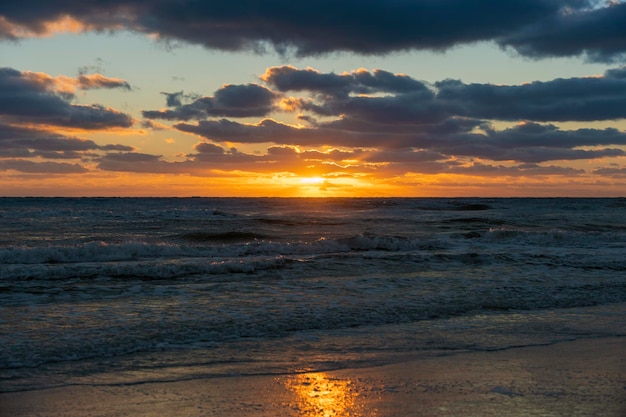 Paesaggio al tramonto sull'oceano con morbide onde di acqua di mare serali che si schiacciano sulla spiaggia sabbiosa