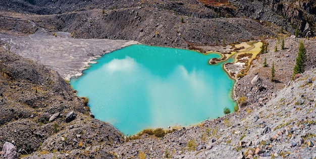 Paesaggio alpino luminoso con lago di montagna nella valle dell'altopiano alla luce del sole e grande montagna sotto il cielo nuvoloso blu. Ombra di nuvole sulla valle di montagna autunnale. Viste panoramiche.